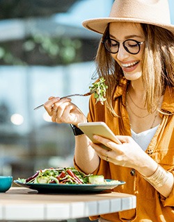 Woman smiling while looking at her phone and eating