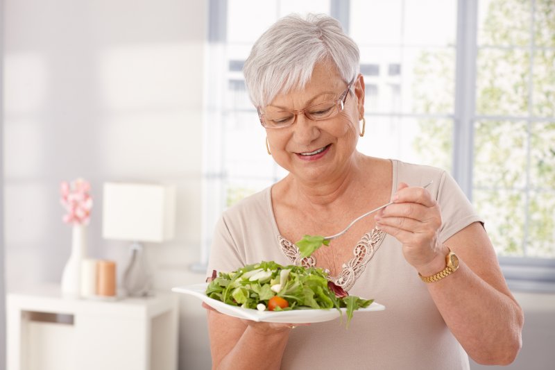 an older woman preparing to eat a salad while wearing dental implants