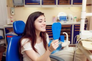 teenage girl seeing her smile in mirror in dental chair 